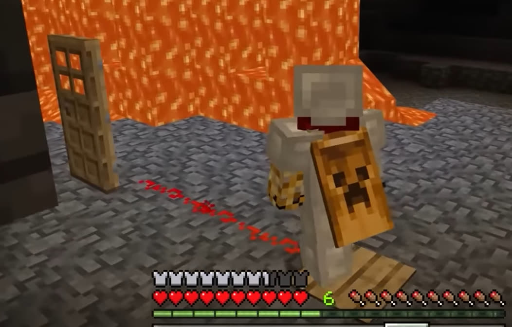 A player in iron armour with a creeper shield in a cave, next to a door and a wall of lava